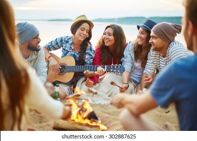 Friendly girls and guys singing by guitar by campfire - Powered by Shutterstock