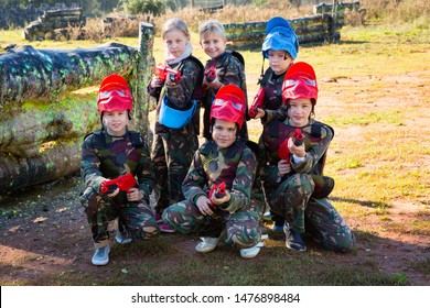 Friendly glad  cheerful positive  group of children paintball players in camouflage posing with guns on paintball playing field outdoors