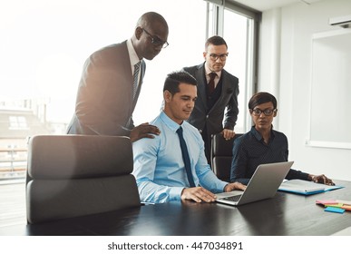 Friendly Group Of Diverse Young Business People In Formal Clothing Looking At Laptop On Conference Table In Front Of Large Window