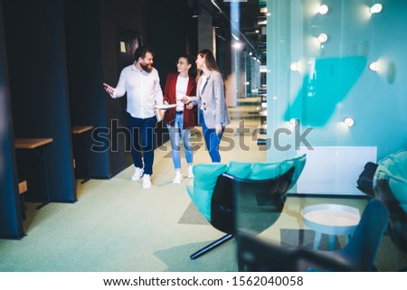 Friendly group of office workers with documents walking along creatively decorated corridor and chatting while gesturing and looking at each other