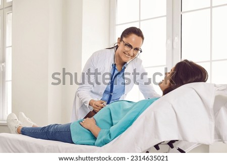 Friendly gynecologist doctor examining heartbeat in the abdomen of pregnant young woman lying on the couch in medical clinic. Obstetrician doctor checking her patient expecting a baby.