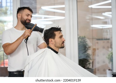 Friendly hair salon specialist blow-drying brunet guy hair at barbershop - Shutterstock ID 2204019139