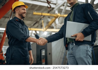 Friendly handshake. Two male factory workers are in the warehouse.