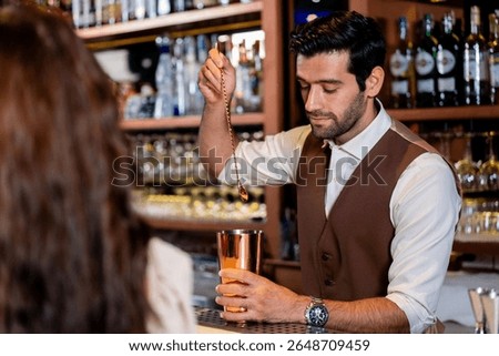 Friendly handsome bartender smiling and talking with a customer while preparing a craft cocktail with a copper shaker. Excellent hospitality and service in a modern lounge at night.