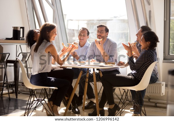 Friendly happy diverse team workers talking\
laughing eating pizza together in office, cheerful workers staff\
group chatting sharing meal enjoying having fun at work, good\
relations at lunch\
break