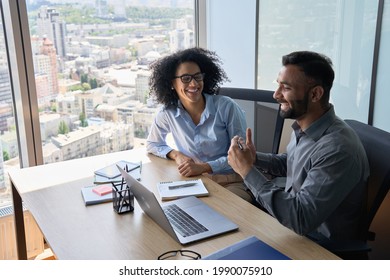 Friendly happy multiethnic coworkers male indian and black female sitting at desk with laptop working together discussing successful project. Corporate business collaboration concept. Top view.