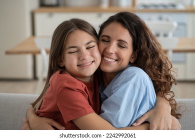 Friendly happy woman and teen girl hug and rejoice at meeting after long separation or going on vacation. Closeup smiling positive mother and daughter hugging each other tightly sits on sofa at home - Shutterstock ID 2242992061