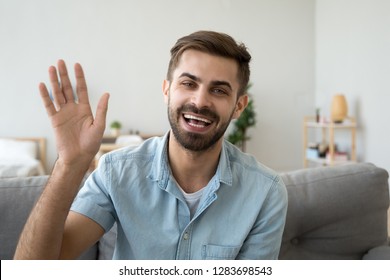 Friendly happy young man waving hand saying hello looking at camera greeting distant friend making online call, cheerful male vlogger blogger recording vlog teaching e-coaching via webcam, portrait