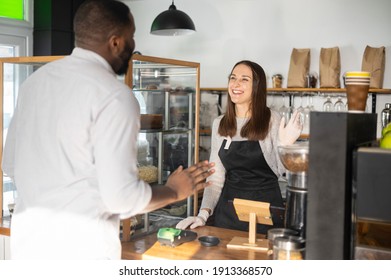 Friendly and helpful waitress is serving an African-American male customer, greeting with cafe client. Female bakery owner glad to see a guest - Powered by Shutterstock