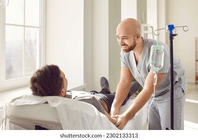 Friendly hospital staff gives intravenous vitamin course infusion to patient. Smiling nurse personnel puts IV line venous needle in vein of relaxed adult male lying and resting on bed in medical ward