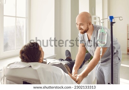 Friendly hospital staff gives intravenous vitamin course infusion to patient. Smiling nurse personnel puts IV line venous needle in vein of relaxed adult male lying and resting on bed in medical ward Stock foto © 