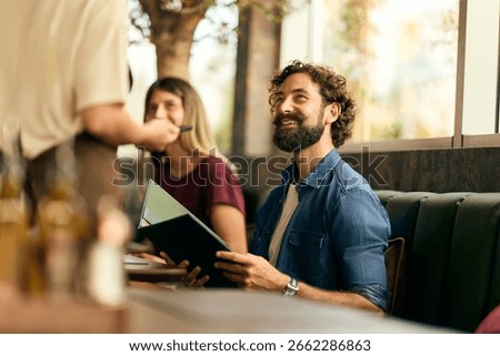 Friendly interaction between a bearded man and waitress at a cozy casual restaurant.