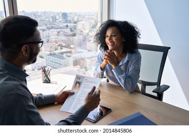 Friendly interview between Indian businessman hr director holding paper cv hiring for job female African American applicant manager sitting in contemporary office. Human resources recruitment concept.
