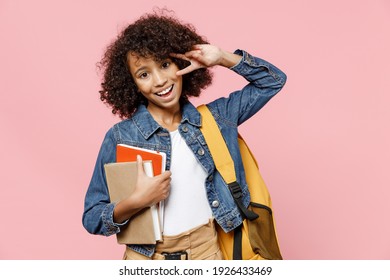 Friendly little african american kid school girl 12-13 years old in casual denim clothes backpack hold books show victory v-sign gesture isolated on pastel pink background Childhood education concept