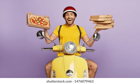 Friendly looking delighted delivery man holds cardboard boxes, one opened container with delicious pizza, transports food items from cafe to clients, brings orders by motorbike, likes his job
