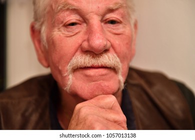 A Friendly Looking Old Man With A Walrus Mustache. A Friendly Elderly Man Is Resting His Head On His Hand.