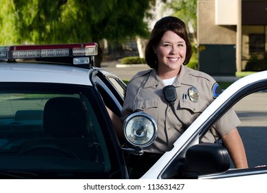 a friendly looking police officer smiles and stands next to her patrol car.