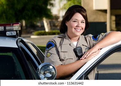 A Friendly Looking Police Officer Smiles And Stands Next To Her Patrol Car.