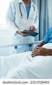 Friendly Male Doctor Talks to Male Patient Resting in Bed. doctor with chart attending sick man in hospital ward. - Shutterstock ID 2311928401