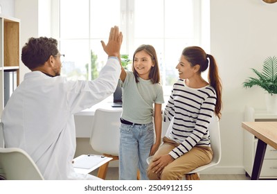 Friendly male pediatrician doctor giving high five to a little child girl patient standing at the doctor's office with her mother during medical examination in clinic. Pediatric medicine concept. - Powered by Shutterstock