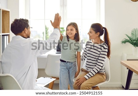 Friendly male pediatrician doctor giving high five to a little child girl patient standing at the doctor's office with her mother during medical examination in clinic. Pediatric medicine concept.