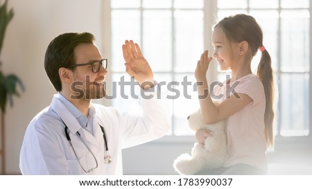 Friendly male pediatrician giving high five to little patient close up, pretty preschool girl hugging favorite fluffy toy greeting friendly doctor gp at meeting, children healthcare concept