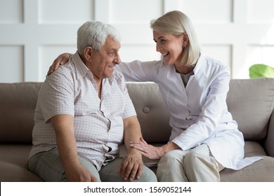 Friendly mature general practitioner communicating with pleasant 80s male patient, sitting together on sofa. Smiling trustful middle aged doctor giving psychological help to elder man at home visit.