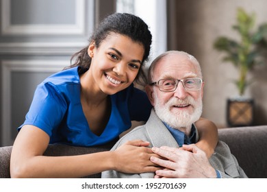 Friendly mature general practitioner communicating with pleasant 80s male patient, sitting together on sofa. Smiling trustful young doctor giving psychological help to elder man at home visit.