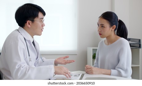 Friendly medic service people or asia male help talk discuss of medical exam record test result at clinic office desk. Young sad serious stress woman visit, follow , listen, see doctor at hospital.