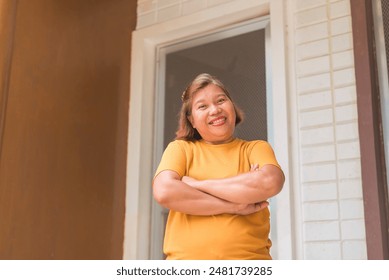 Friendly middle aged asian woman standing in front of her apartment flat, arms crossed. - Powered by Shutterstock