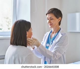 Friendly middle-aged woman doctor wearing gloves checking sore throat or thyroid glands, touching neck of young African female patient visiting clinic office. Thyroid cancer prevention concept - Shutterstock ID 2026641008