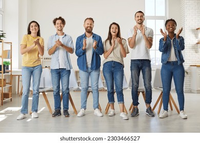 Friendly multiracial people in casual clothes stand in row and applaud looking at you. Group of friends in jeans and T-shirts joyfully clap their hands while standing in row in room. Team concept. - Powered by Shutterstock