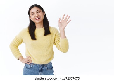 Friendly Nice Asian Woman In Yellow Sweater Greeting Friends, Waving Hand In Hi, Hello Gesture And Smiling Carefree, Welcoming New People To Their Multicultural Team At Work, Helping Out Start Career