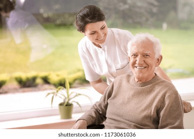 Freundliche Krankenschwester, die behinderte lächelnde ältere Menschen im Pflegeheim unterstützt