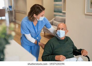 Friendly nurse wearing protective face mask helping handicapped senior man in wheelchair at hospital during covid19 pandemic. Nurse with surgical mask taking care of an elderly patient on a wheelchair