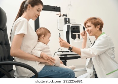 Friendly ophthalmologist checking child ocular health in presence of mother