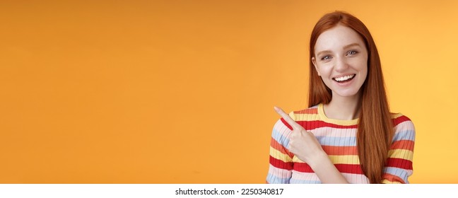 Friendly outgoing good-looking ginger girl university student discussing lecture classmate smiling laughing pointing upper left corner questioned curious know details standing orange background.