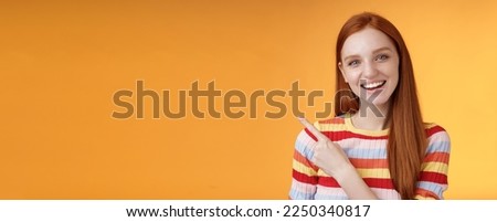Friendly outgoing good-looking ginger girl university student discussing lecture classmate smiling laughing pointing upper left corner questioned curious know details standing orange background.