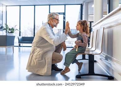 Friendly pediatrician giving high five to little patient. Cute preschool girl in greeting doctor in hospital corridor. - Powered by Shutterstock