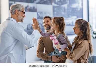 Friendly pediatrician giving high five to little patient. Parents with girl patient greeting doctor in hospital corridor. - Powered by Shutterstock