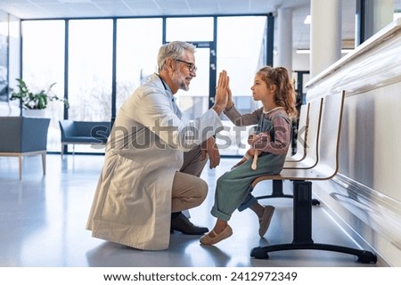 Friendly pediatrician giving high five to little patient. Cute preschool girl in greeting doctor in hospital corridor.