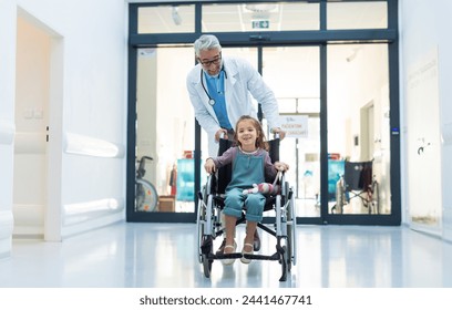 Friendly pediatrician pushing little patient in wheelchair. Cute preschool girl trusting her healthcare workers in hospital. - Powered by Shutterstock