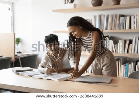 Friendly peer learning. Two young diverse multiethnic students mates engaged in self studying at library discuss books review scientific literature. Teen girl help male groupmate in writing coursework