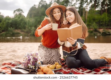 Friendly picnic on the beach. Two girlfriends enjoy a picnic by the river on a sunny day.  Concept of relaxation, nature, travel.