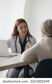 Friendly positive doctor woman seeing patient in office, speaking to elderly lady at work table with laptop, explaining checkup result, examination, treatment, making hand gestures. Vertical shot - Shutterstock ID 2261002249
