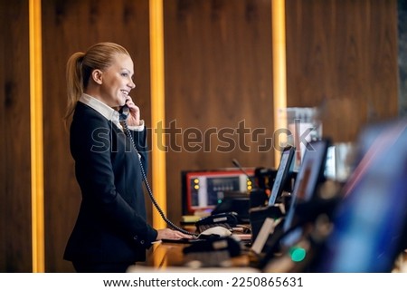 A friendly receptionist at reception is talking on the phone with hotel guest.