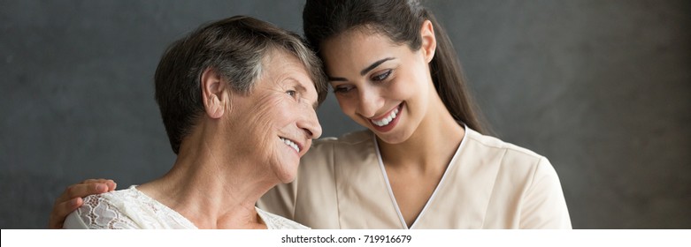 Friendly Relationship Between Smiling Caregiver In Uniform And Happy Elderly Woman