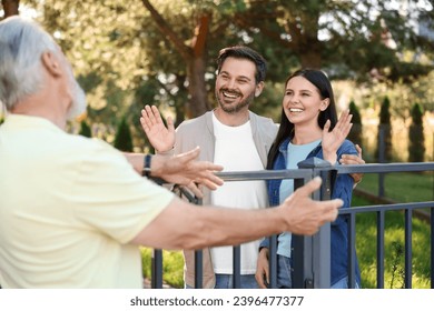 Friendly relationship with neighbours. Happy couple greeting senior man near fence outdoors - Powered by Shutterstock