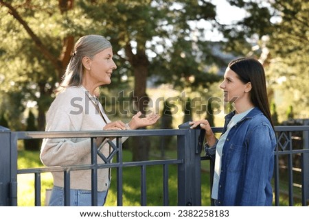Friendly relationship with neighbours. Happy women talking near fence outdoors Stock foto © 