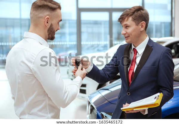 Friendly salesman\
giving car keys to his client. Man buying new automobile, receiving\
car keys from car\
dealer